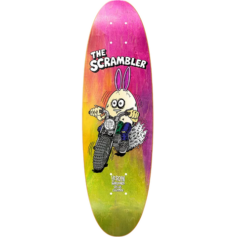 A long skateboard deck featuring a vibrant pink, orange, and yellow gradient design with a cartoon rabbit riding a motorcycle. The words 'THE SCRAMBLER' are printed above the illustration, and 'HERON' is visible near the bottom.